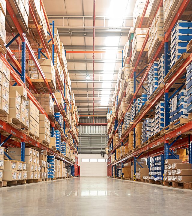 Rows of shelves with goods boxes in huge distribution warehouse at industrial storage factory.